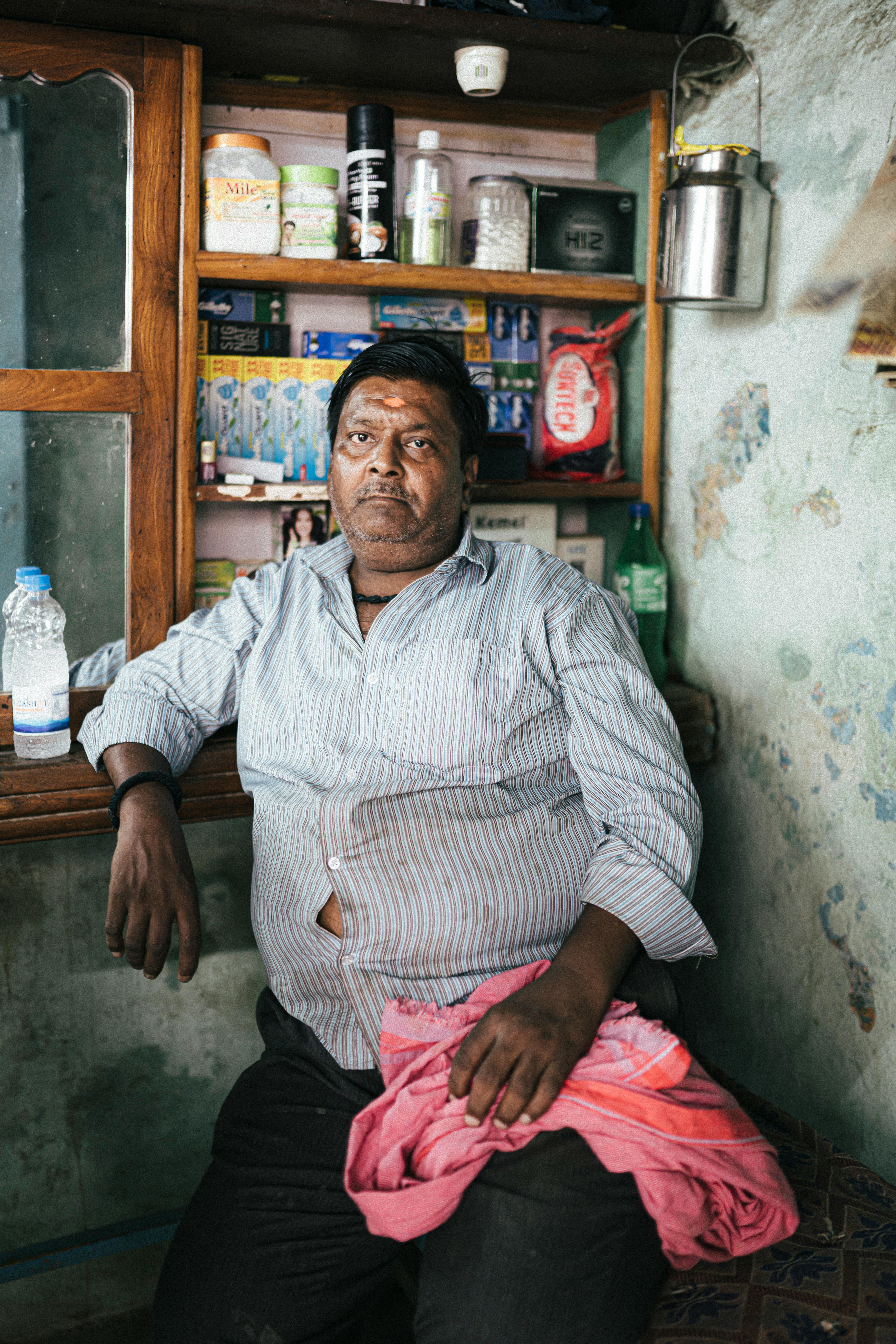 A candid portrait of a man sitting inside a shop in Varanasi, India, displaying local common goods.