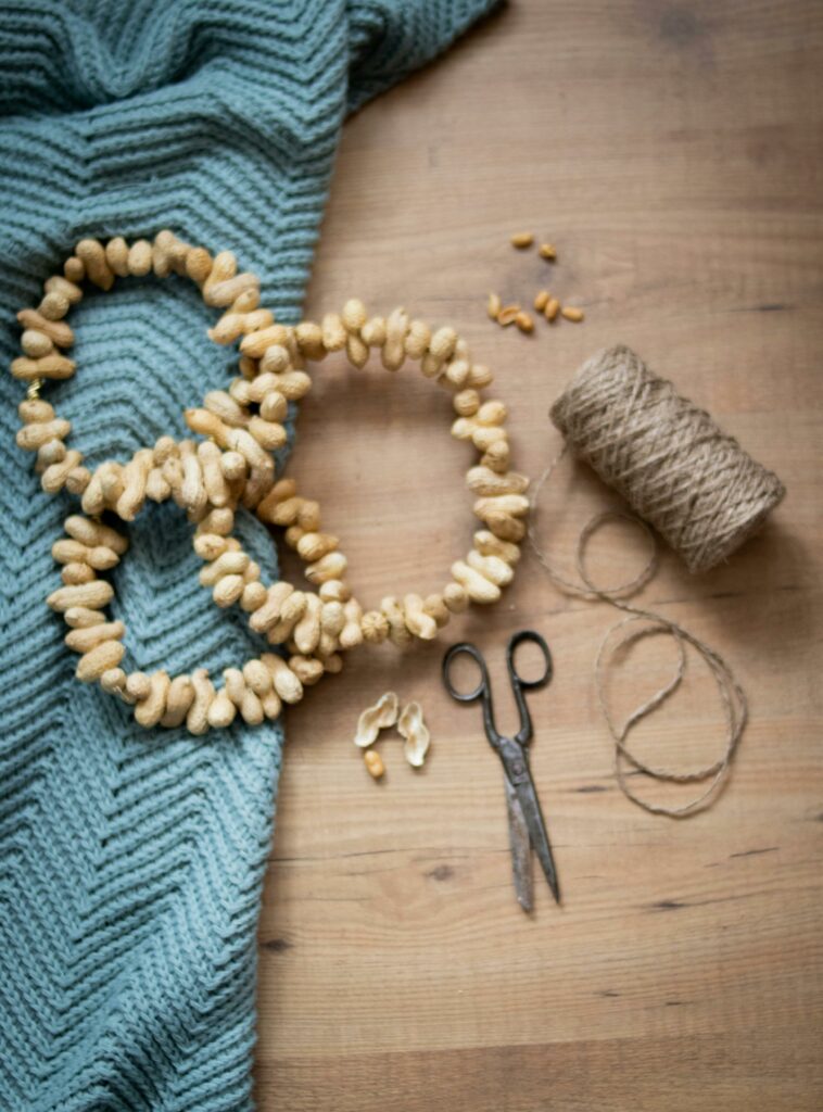 Flat lay of a peanut garland, scissors, and yarn on wood, perfect for a creative DIY project.